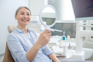 senior patient observing smile in hand mirror