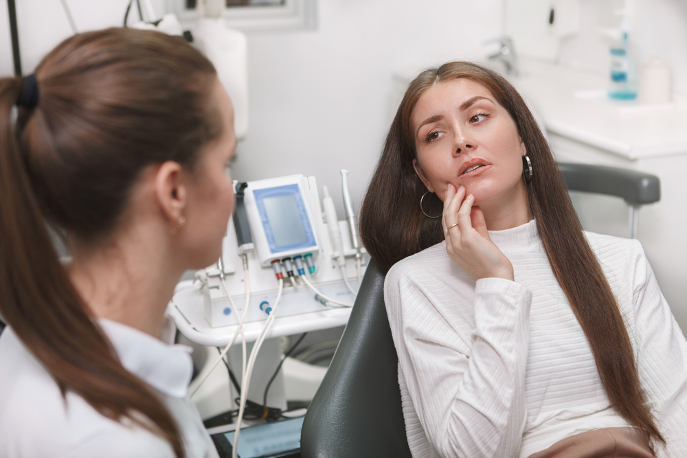 patient in dental chair holding jaw in pain speaking to dentist